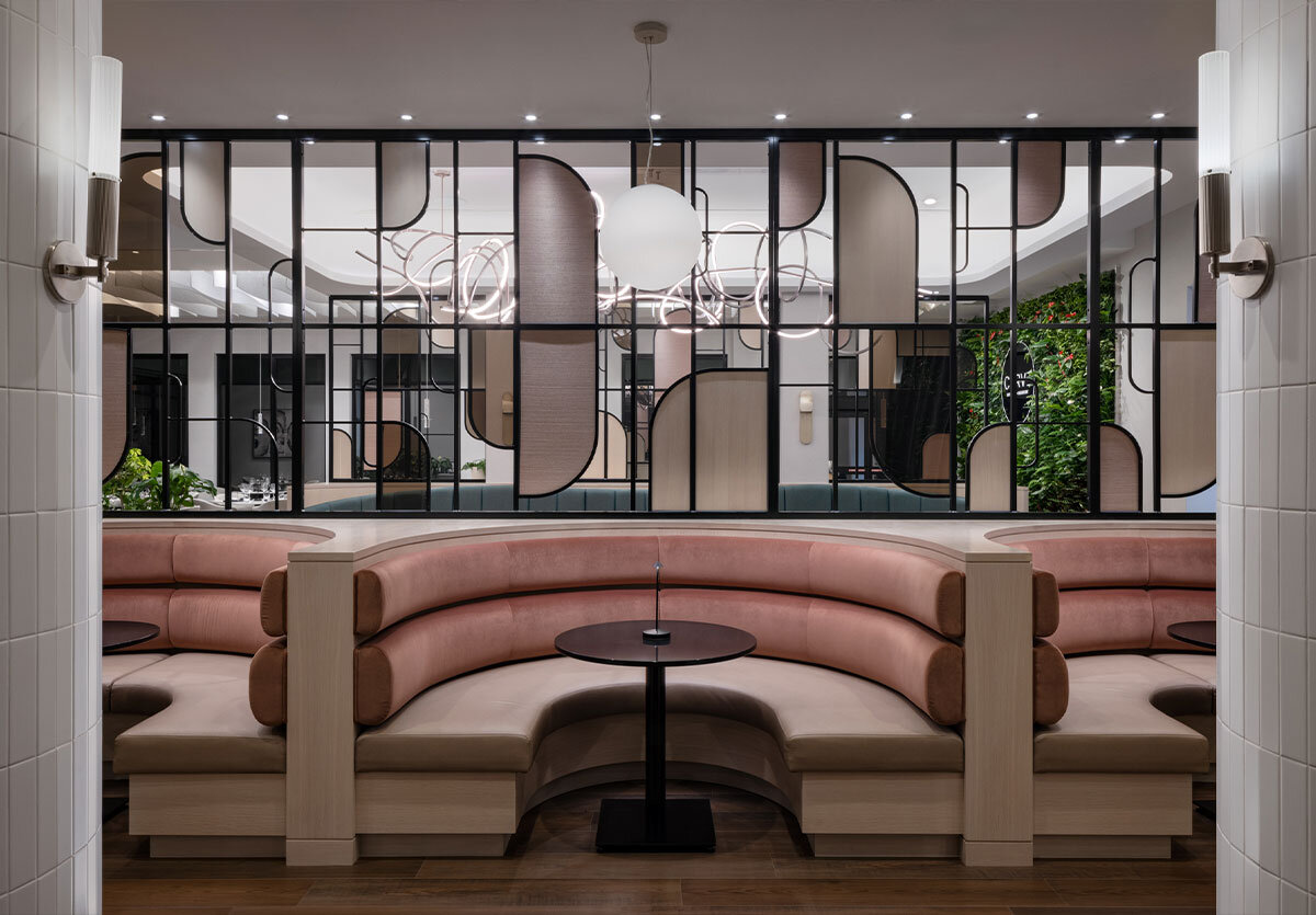 A glimpse inside the neutral coloured restaurant with tables for 4 with modern, c-shaped dining chairs, overlooking outside