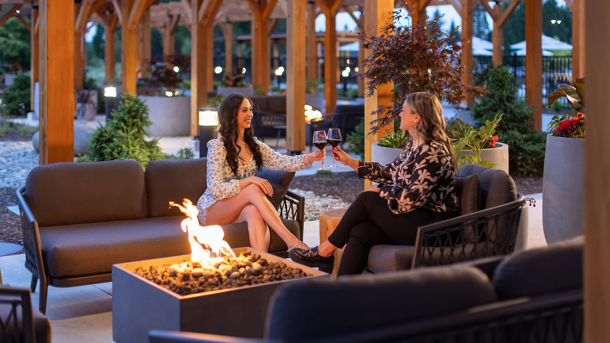 A glass of white wine sits on a fire table with lounge chairs in the background out of focus.